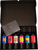 Sechs Flaschen mit bunten Etiketten sind in einer schwarzen Box angeordnet. Eine kleine graue Karte liegt oberhalb der Flaschen. Die Umgebung ist schlicht und elegant.