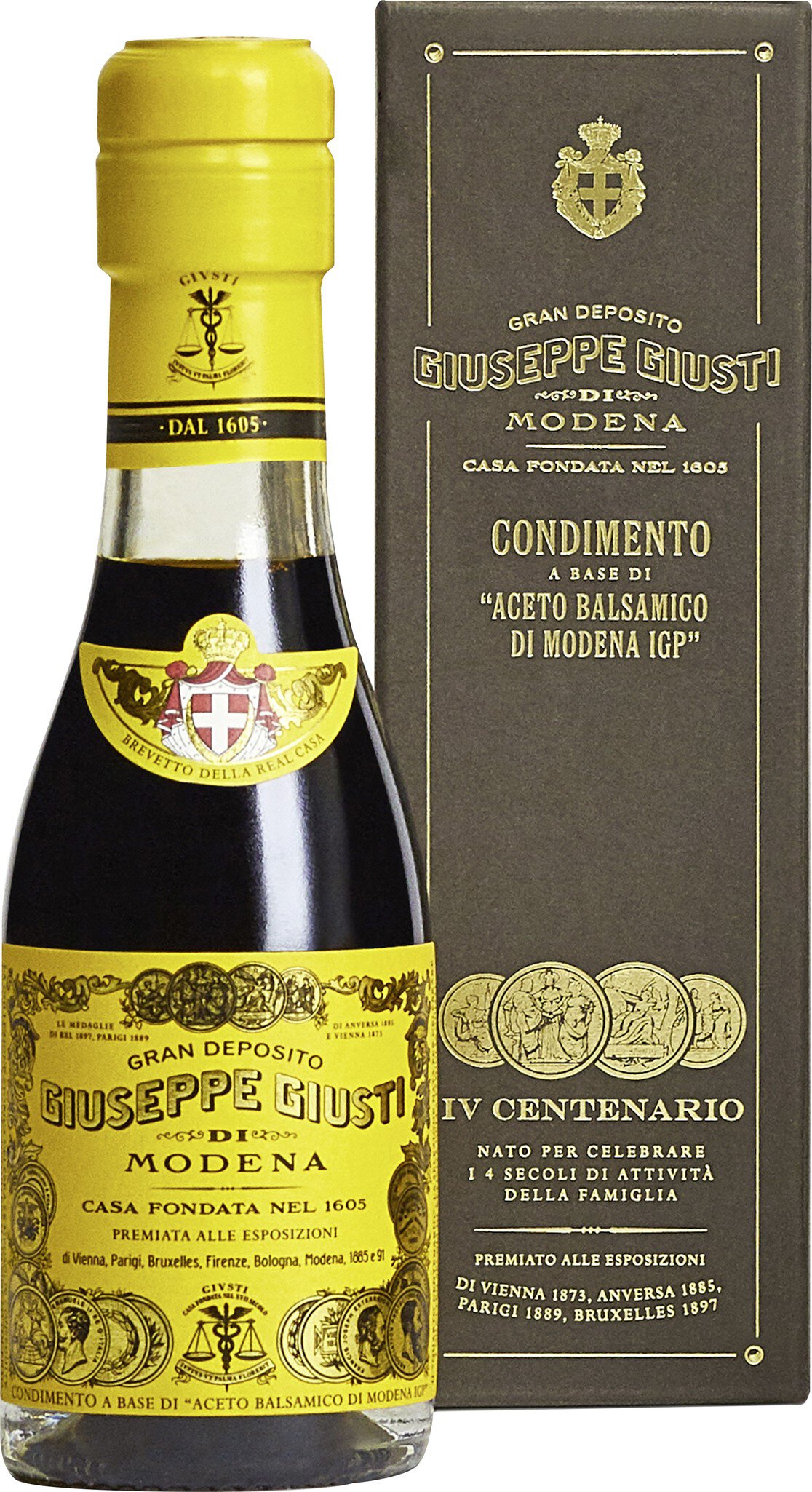 Eine Flasche Balsamico-Essig steht vor einem beige-farbenen Hintergrund. Die Flasche hat ein gelbes Etikett mit goldenen Details und zeigt ein traditionelles Muster.