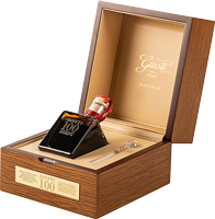Eine luxuriöse Holzschatulle ist geöffnet und zeigt eine elegante, schwarze Box in Form eines Quadrat-Pyramide mit einem glänzenden, roten Objekt darauf. Innerhalb der Schatulle ist eine feine, cremefarbene Innenauskleidung sichtbar.